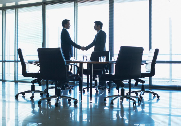 Two men in business suits shaking hands in a conference room.