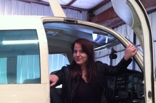 Young woman sitting in a parked aircraft with the door open, smiling
