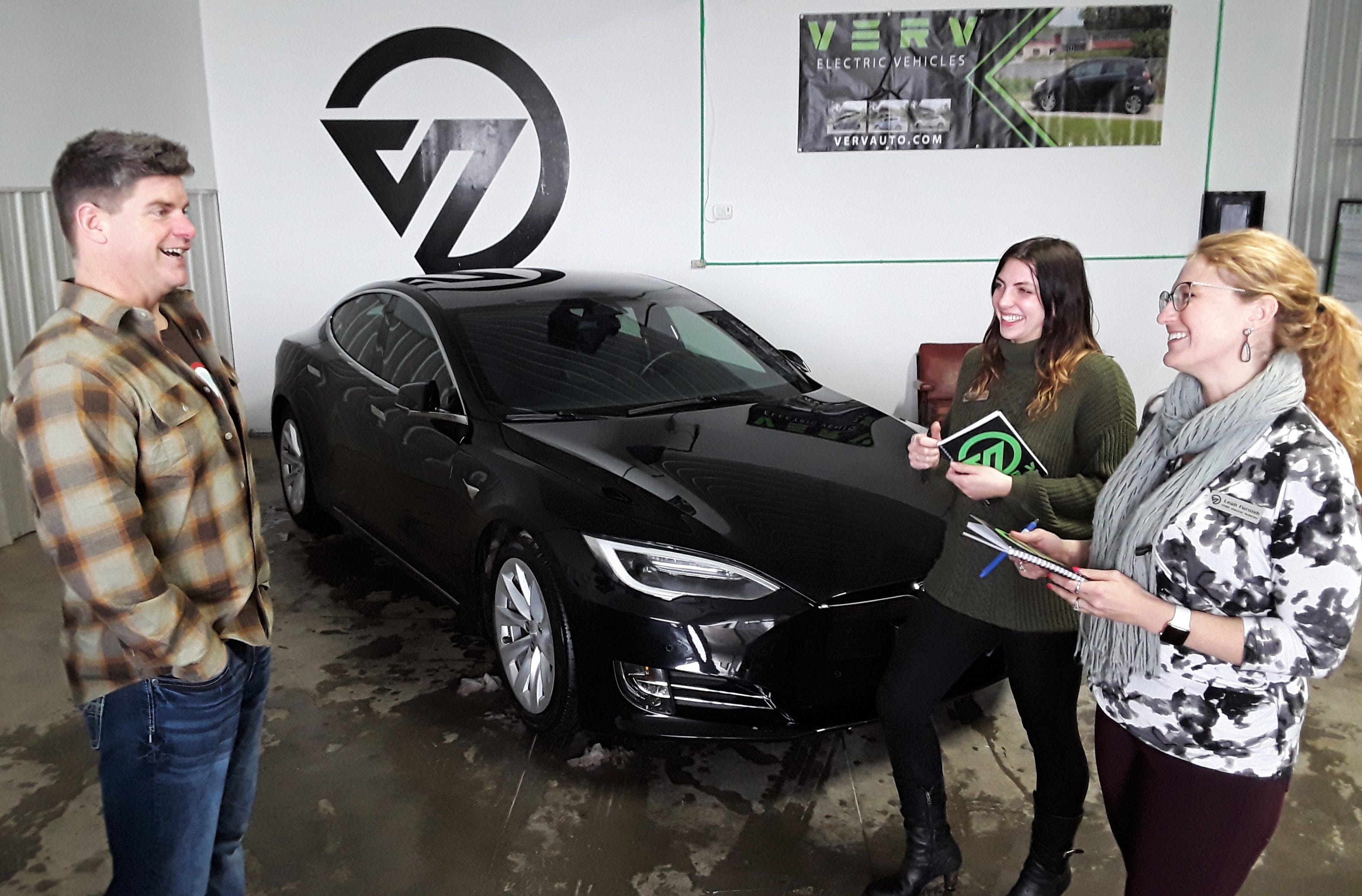 VERV CEO and owner Jason Hall jokes with his two employees Tessa Meyer (left) and Leah Furnish next to the premier vehicle in their current used electric car inventory – a sleek, black 2018 Tesla Model S. The owner says the dealership is a logical spin-off from his Moxie Solar company in North Liberty.
