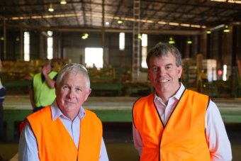 Two men in working shirts smile for the canmera