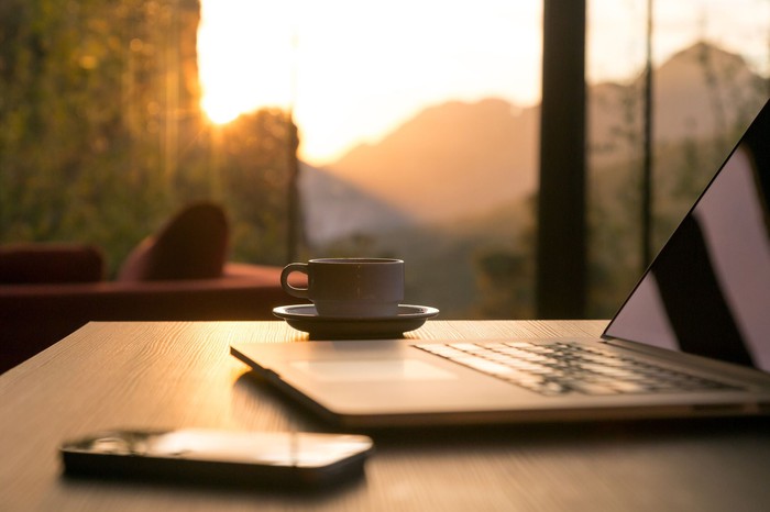 A smartphone, laptop, and cup of coffee sitting on a desk.